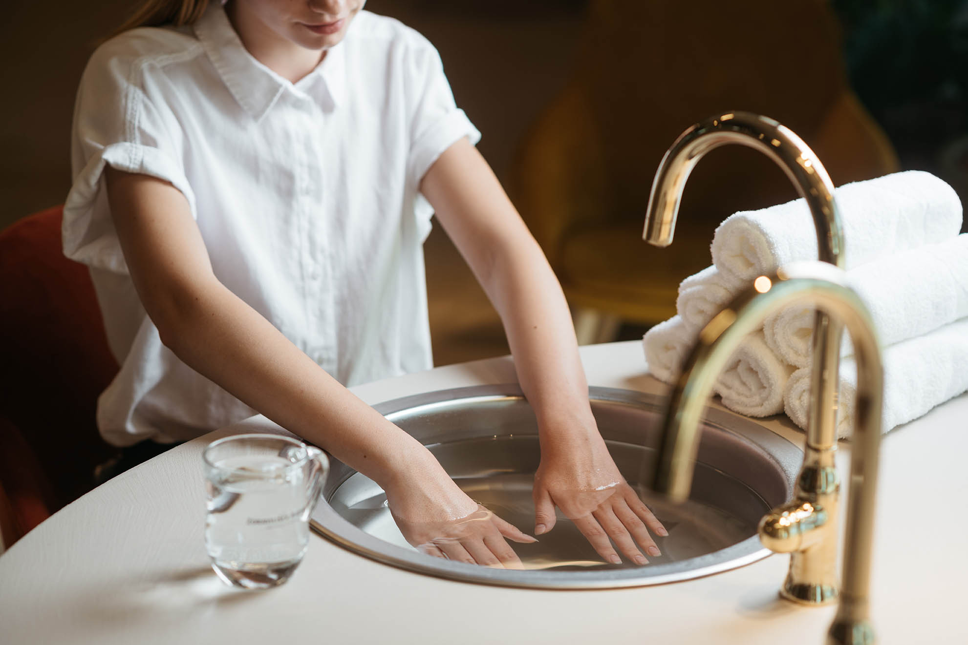 Ženska v beli srajci namaka roke v umivalnik, ki je poln vode