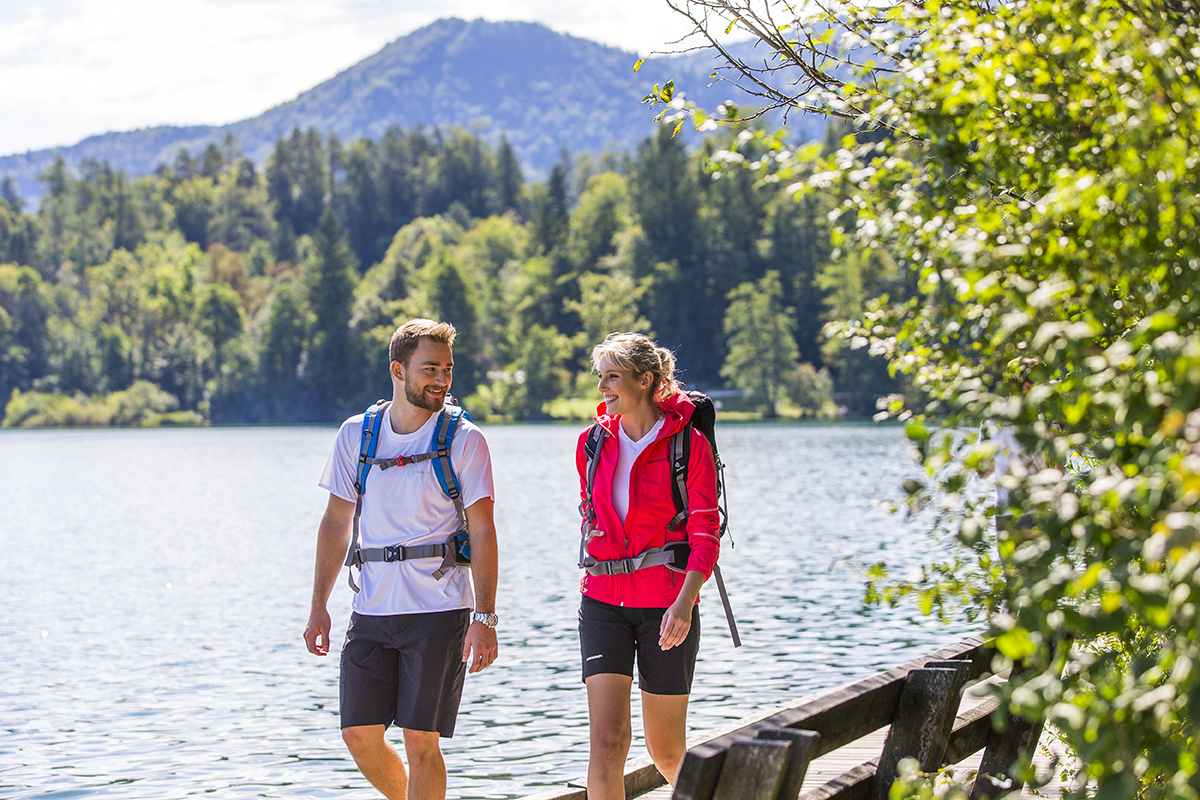 Moški in ženska v športnih oblačilih in s pohodniškim nahrbtnikom pešačita na potki okrog jezera