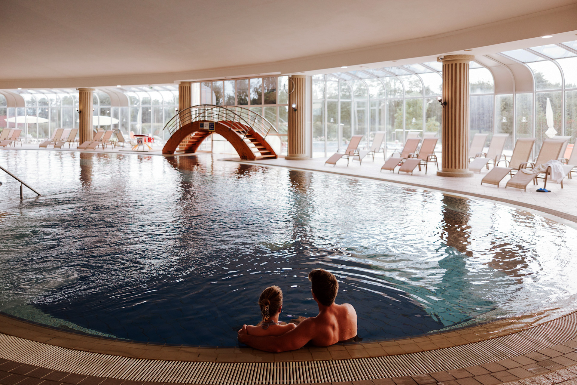 Moški in ženska se v kopalkah sprehajata ob robu notranjega bazena termalne riviere