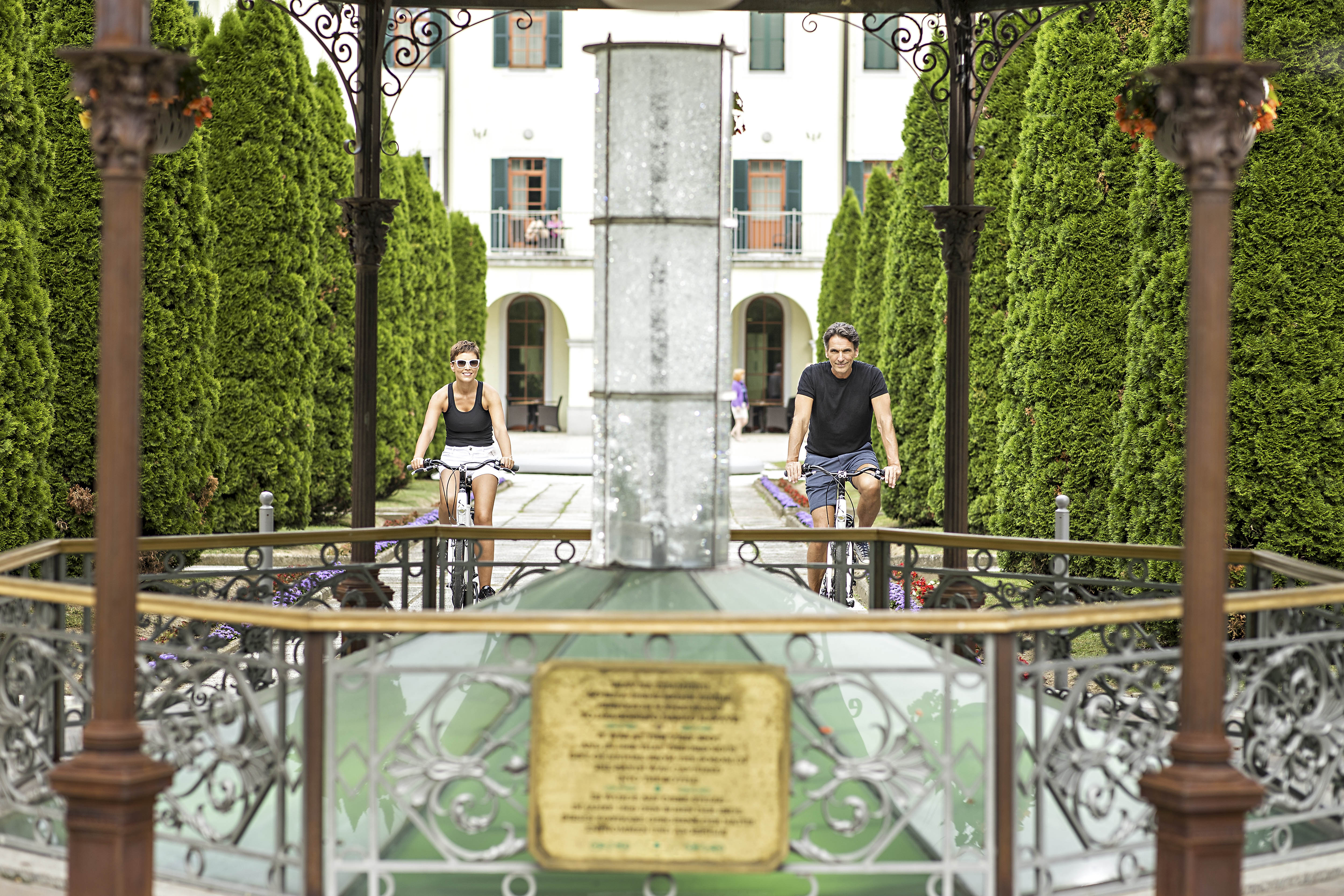 Moški in ženska v športnih oblačilih  kolesarita v zelenem parku ob termalnem vrelcu