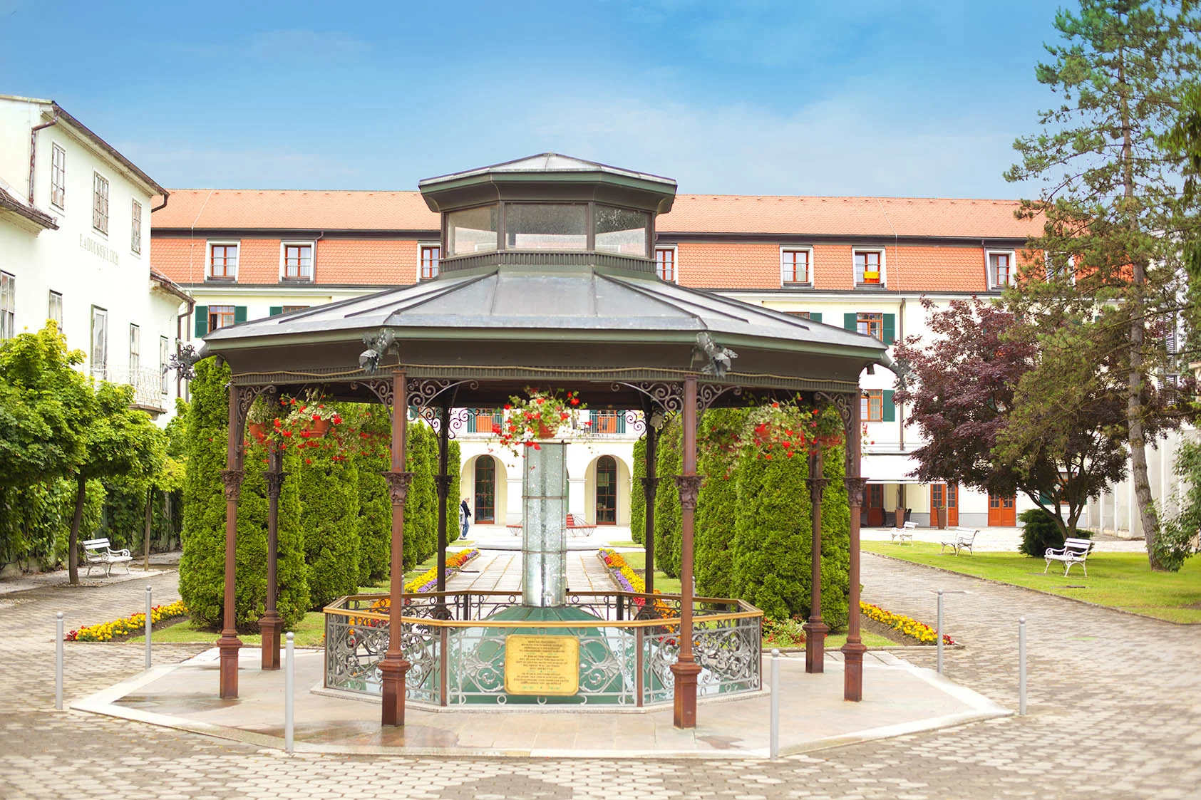 Lepo urejen zelen park z mineralnim vrelcem v ospredju in sprehajalnimi potkami